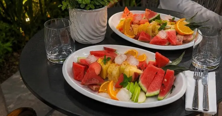 Two platters of sliced watermelon, pineapple, orange on outdoor table