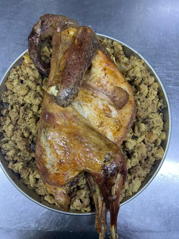 Whole roasted fowl centred on bread stuffing in metal tray