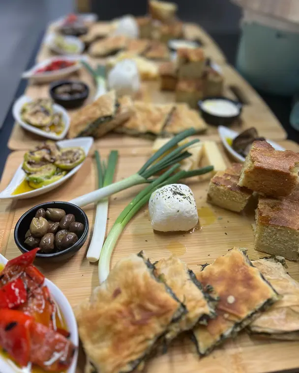 Wooden board with pastries, cheese, olives, spring onions and peppers