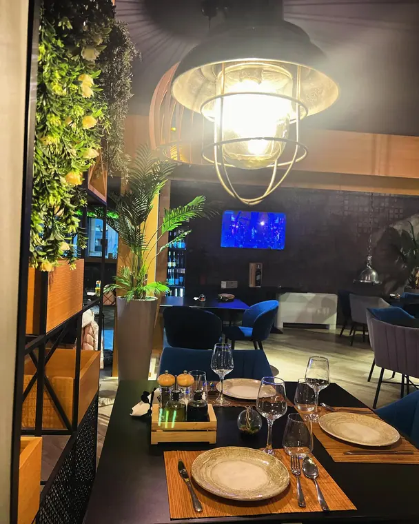 Dining room at night with pendant lamp, set tables and potted palms
