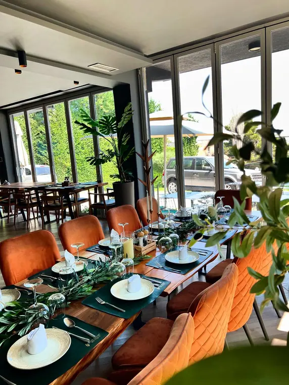 Dining room tables set with olive-branch runners beside folding glass doors