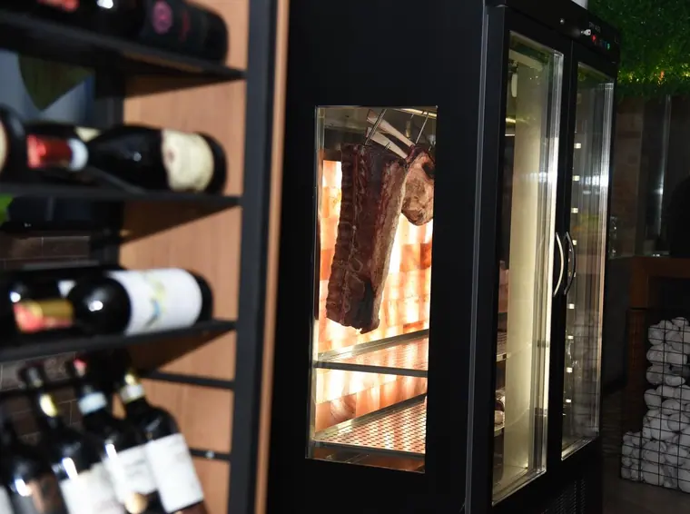 Dry-aging cabinet with beef rib beside a wine rack