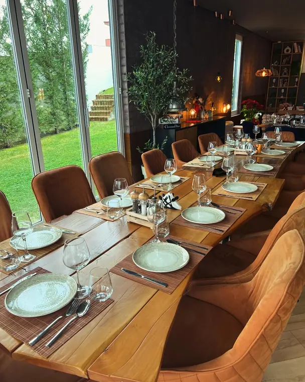 Long wooden dining table set for many guests beside garden windows