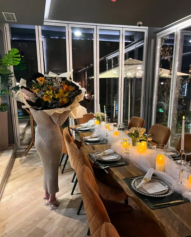 Person holding large flower bouquet beside candlelit set dining table
