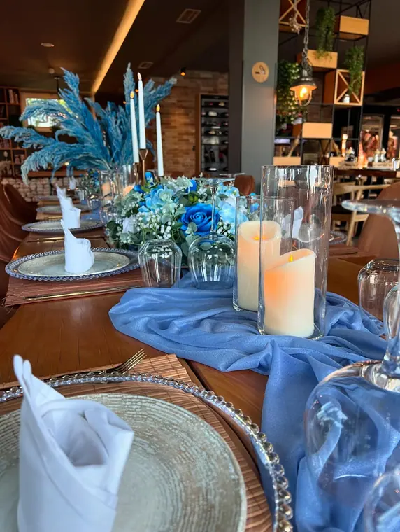 Place settings with candles and blue roses along a wooden table