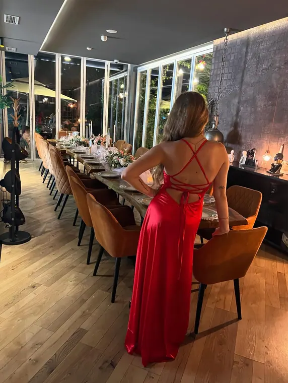 Woman in red gown seen from behind beside long set dining table
