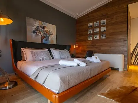 Bedroom with tan leather bed, wood panel wall and framed prints